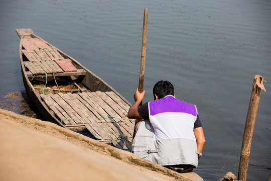 Young man getting ready to sail the wooden boat to the river. Young boy holding the paddle of the boat to float on the lake by wooden boat. Man sitting on the boat.