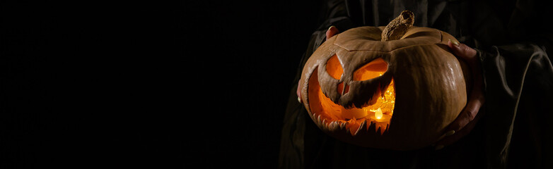The witch is holding a pumpkin jack o lantern glowing in the dark. Halloween.