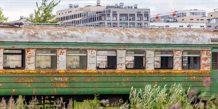 An old passenger railway car with peeling paint in the city on the background of houses and buildings.  An empty carriage on the railway.