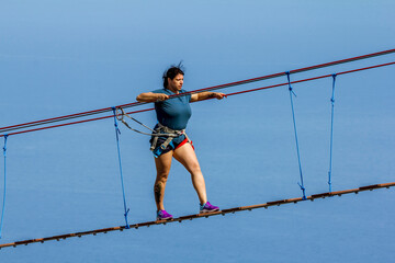 Young woman crossing a chasm on a rope bridge - obrazy, fototapety, plakaty