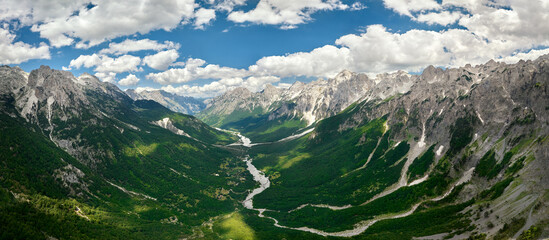 Panoramic, aerial view of the Valbone river valley, green valleys, blue sky with clouds, steep rocks, remnants of snow. Hikers paradise. Theth national park, Albanian Alps, Albania.
