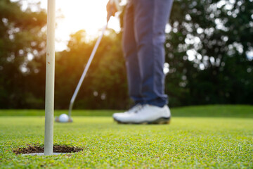 Golfer putting ball on the green golf, lens flare on sun set evening time.
