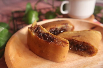 Sweet chocolate flavored martabak served on a wooden plate and accompanied by a glass of warm tea