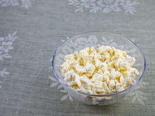 Cottage cheese in a glass bowl on the background of a gray tablecloth.