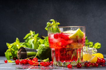 Red currant lemonade or mojito cocktail. Iced fresh summer cocktail with currant berry, lime, miint and ice cubes. Dark tiled background copy space