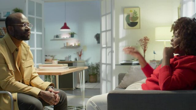 African American wife sitting on couch in living room and explaining her feelings to husband while resolving conflict at home