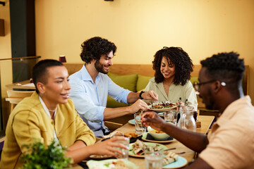 Multicultural friends are sitting in a restaurant, eating food and talking.