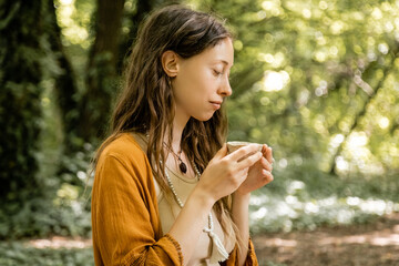 Side view of young woman holding tea bowl in forest.