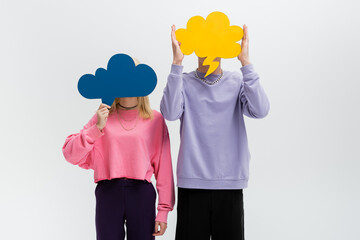 Young couple holding thought bubbles near faces isolated on grey.
