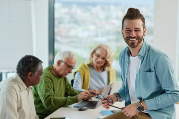 A group of senior students sit in a classroom with their teacher and work on a school project.