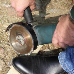 Handy grinder with a circular saw next to foot closeup - safety when working with a DIY manual power tools
