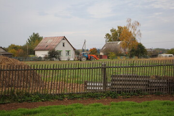 West Russian rural landscape with rustic houses, potato seeder tractor, green field, hay stack and old wooden fence at spring day