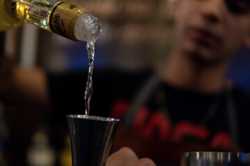 A bartender poured tequila into a shaker to prepare a shot. Unfocused waiter. Bartender's hands...