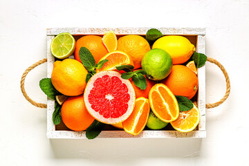 Fresh citrus fruits with leaves: lemons, oranges, mandarins, grapefruit, lime in wooden box