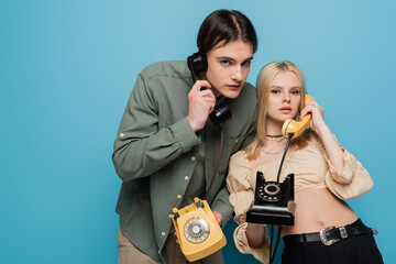 Stylish couple talking on retro telephones and looking at camera on blue background.