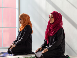 Two Muslim women praying and meditating at home.