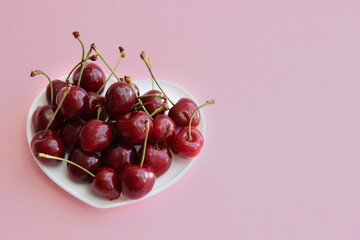 A lot of cherries on a white plate in the form of a heart on a pink background