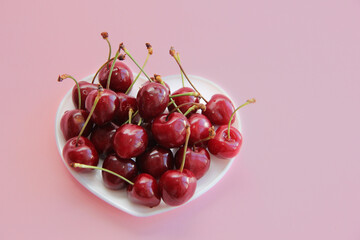 A lot of cherries on a white plate in the form of a heart on a pink background