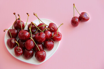 A lot of cherries on a white plate in the form of a heart on a pink background
