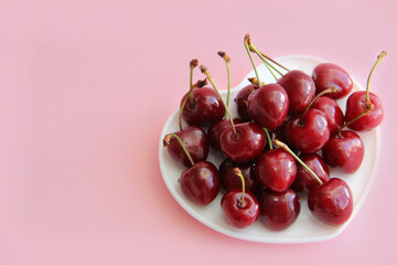 A lot of cherries on a white plate in the form of a heart on a pink background
