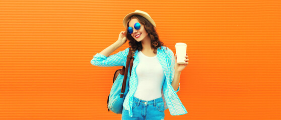 Portrait of happy smiling young woman with coffee cup wearing summer straw hat and backpack on orange background, blank copy space for advertising text