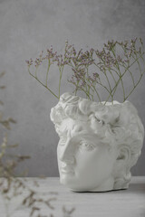 Close-up of an ancient Greek sculpture. Minimal artistic flower poster. White copy of a plaster statue of the head of David on a gray concrete background. vertical position.
