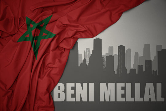 abstract silhouette of the city with text Beni Mellal near waving colorful national flag of morocco on a gray background.