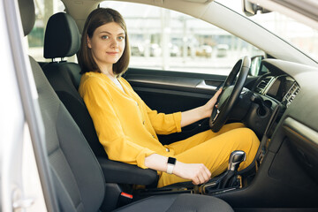 Woman driver driving a car. Safety and people concept. Young female driver driving car in city. Portrait of girl fasten seat belt in her car. Protection of person in vehicles