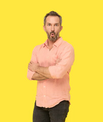 Amazed facial expression middle aged grey haired man standing with arms folded happy looking at camera wearing pink shirt isolated on yellow background. Mature fit man, healthy lifestyle concept