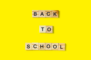 The inscription on the wooden squares in English letters is Back to school. It lies on a yellow background.