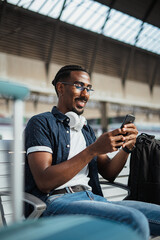Portrait of african man using his phone while he is waiting on a bench at a train station