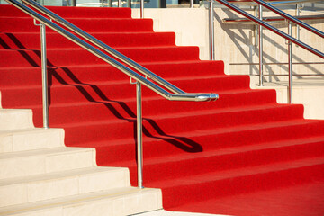 Red carpet on the stairs in a luxury interior outside outdoors and chromed shiny metal railings.