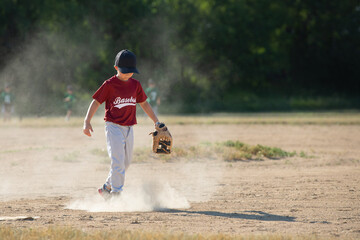 A little boy playing baseball kicking up dirt wearing a baseball glove