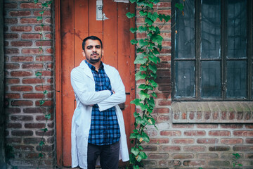 Fototapeta na wymiar South asian young confident male doctor in white apron, Bangladeshi muslim medical student, protection from corona virus and flu viruses