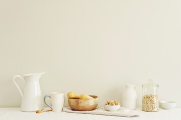 Breakfast concept, natural and white color composition with kitchen utensils on table with white linen tablecloth, empty wall mockup for design, wall art or text.