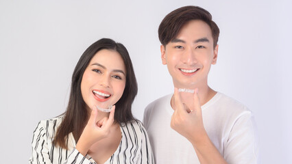 Young smiling man amd woman holding invisalign braces over white background studio, dental healthcare and Orthodontic concept..