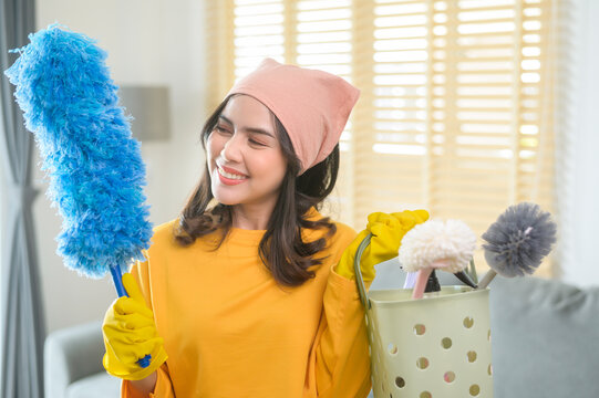 Young happy woman wearing yellow gloves  and holding a basket of cleaning supplies in living room.