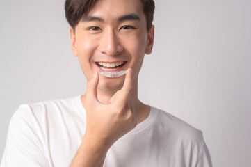 Young smiling man holding invisalign braces over white background studio, dental healthcare and Orthodontic concept..