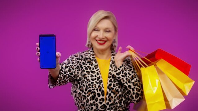 Stylish senior woman showing phone with pre-keyed screen and shopping bags