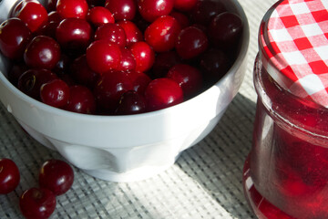 Cherries and a jar of jam on background and fresh fruits on the table, closeup