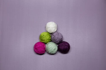 Balls of multi-colored woolen threads for knitting in the form of a pyramid lie on a purple background
