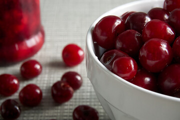 Cherries and a jar of jam on background and fresh fruits on the table, closeup