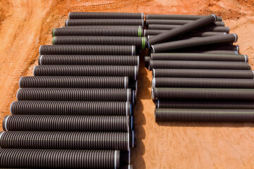 PVC new black plastic pipes stacked in rows at construction site on reconstruction of the city...