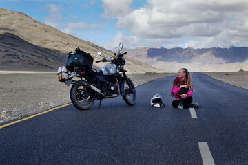 Female biker sitting on perfect road near motorcycle in amazing Himalayas mountains