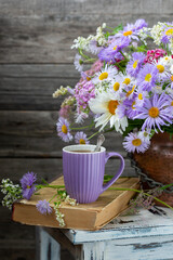 A cup of tea with a summer bouquet of garden flowers with chamomile and Aster alpinus, retro style