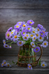 A bouquet of alpine aster in a vase on an old wooden table. Country style