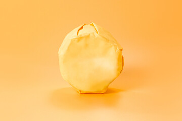 Wrapped unopened paper package of a whole head of camembert on an orange background. Soft. Dairy....