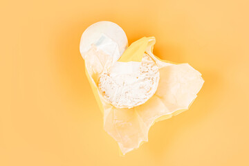 Top view of an open paper package of a whole head of camembert on an orange background. Round. Nutrition. Calcium. Milk. White. Circle. Whole. Breakfast. Mold. Appetizer. Fresh. Product