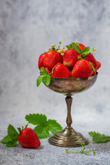 Ripe strawberries in an old silver vase on a gray background.