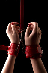 BDSM outfit for adult sex games. Close-up of female hands with red manicure chained with red...
